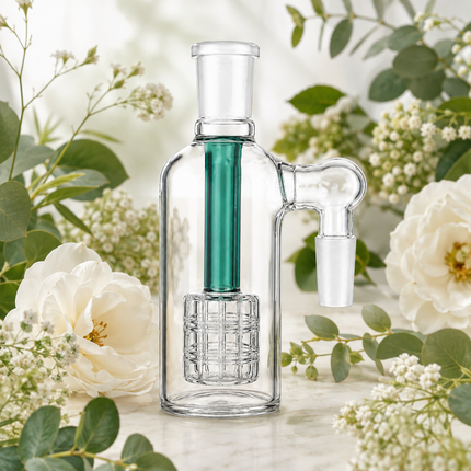 A clear glass water pipe with a green inner tube and white glass mouthpiece, styled with white flowers and green leaves on a light marble surface.