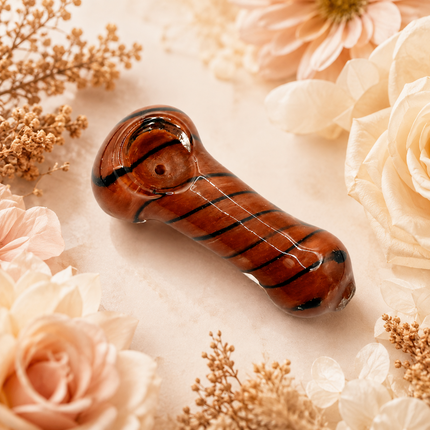 Red brown striped glass spoon hand pipe displayed on a soft floral background