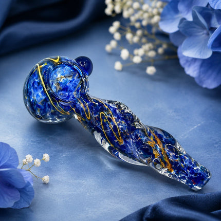 Navy blue crackle glass spoon pipe displayed on a dark blue floral setting with soft white blossoms