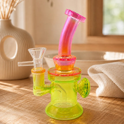 Neon yellow and pink mini glass bong styled in a warm indoor setting with soft natural light and a clean tabletop background