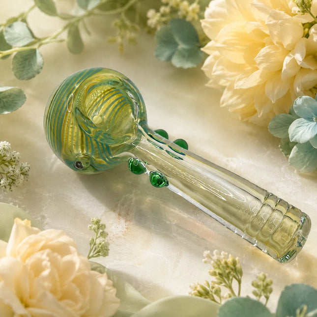 Lime and emerald glass spoon pipe arranged among soft cream flowers with green accents and a warm botanical backdrop