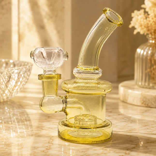 Gold-tinted mini glass bong styled on a warm tabletop with soft lighting and neutral decor in the background