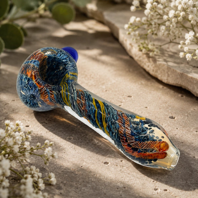 Sapphire blue and yellow web twist spoon pipe displayed on a natural stone surface with warm outdoor lighting