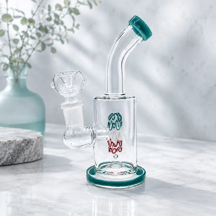 Clear mini glass bong with deep teal accents and a 14mm bowl styled on a light stone surface with a soft white floral background