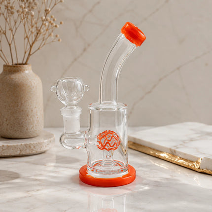 Clear orange dome perc mini glass bong displayed on a neutral tabletop with soft decor and warm natural lighting