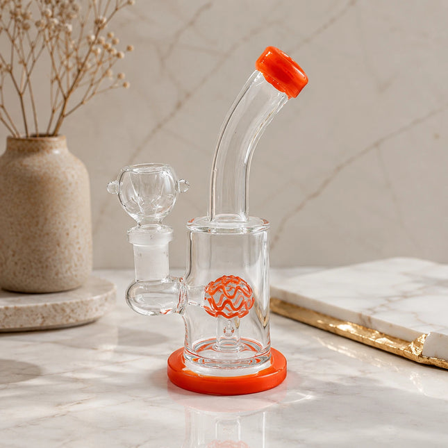 Clear orange dome perc mini glass bong displayed on a neutral tabletop with soft decor and warm natural lighting