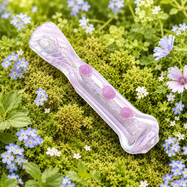 Soft pink glass chillum pipe with raised dot grips displayed on green moss among small blue and white flowers
