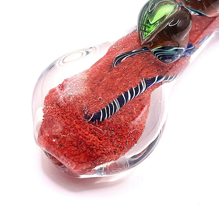 Diagonal side view of the 4-inch glass spoon pipe highlighting the curved red body, clear underside, and swirling linework