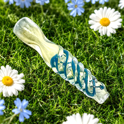 Teal-accented clear chillum arranged on fresh grass beside white daisies and small blue flowers.