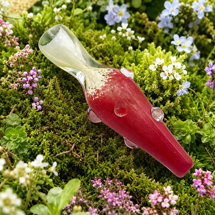 Ruby red chillum resting among moss and tiny wildflowers, with a clear flared mouthpiece and glossy raised grip dots