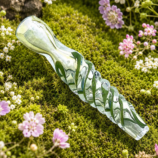 Green spiral glass chillum pipe with clear mouthpiece displayed on a mossy floral background with pink and purple flowers