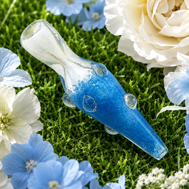 Blue glass chillum pipe with clear mouthpiece and raised dot accents displayed on a floral grass background