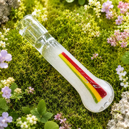 Clear chillum with red, yellow, and black Rasta-style stripes photographed on a mossy floral background with tiny spring blossoms.
