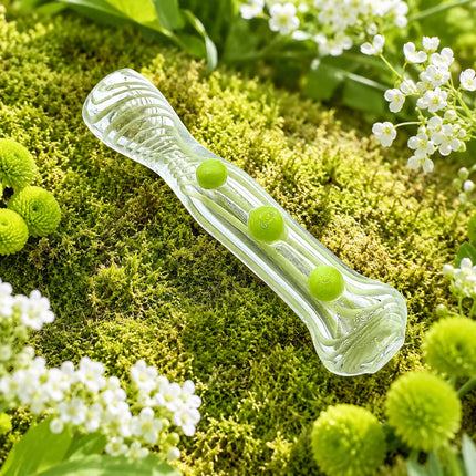 Clear 3-inch spoon pipe displayed on a fresh moss garden backdrop with bright melon green grip dots and small white flowers.